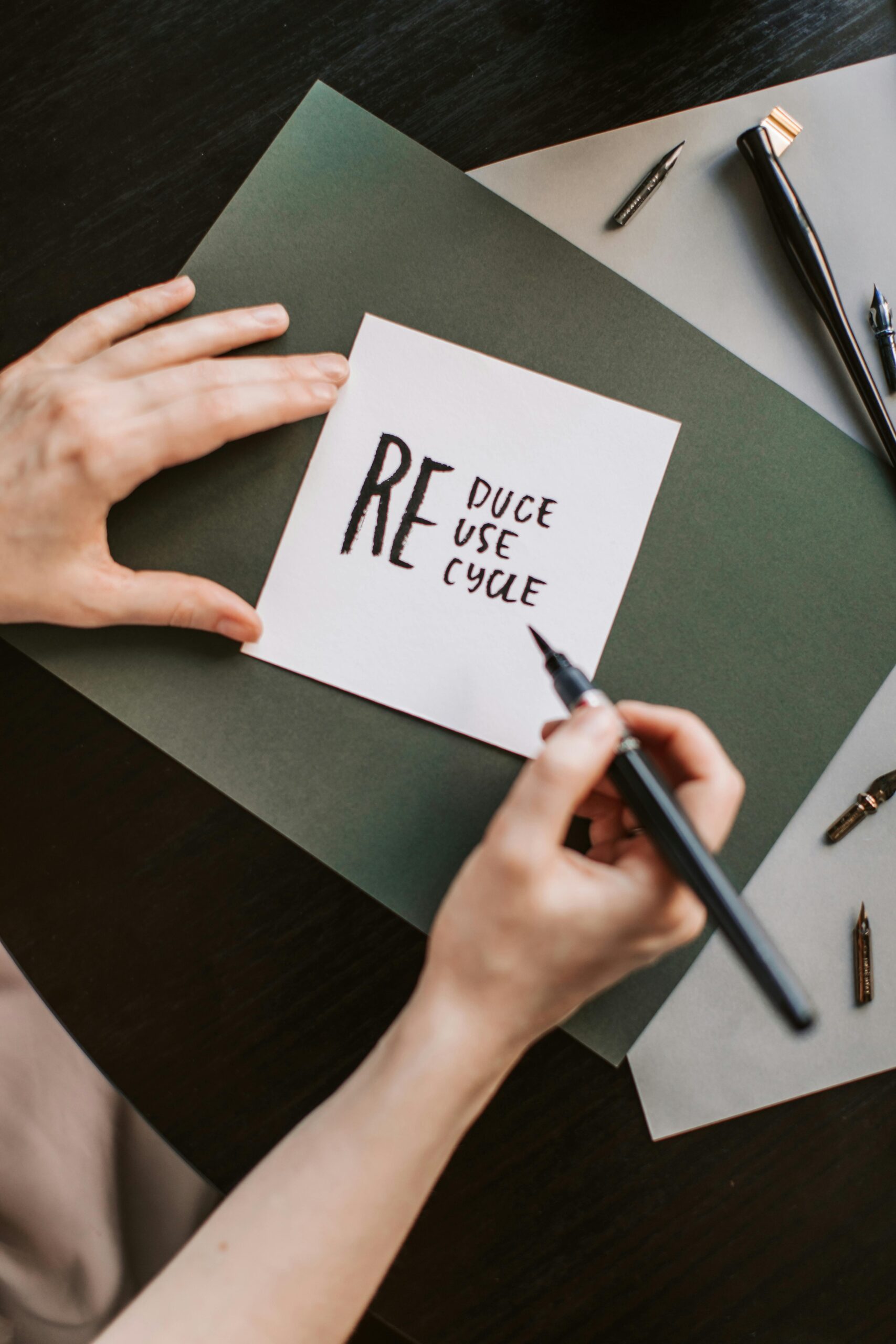Close-up of hands writing 'reduce, reuse, recycle' on paper, promoting sustainability.